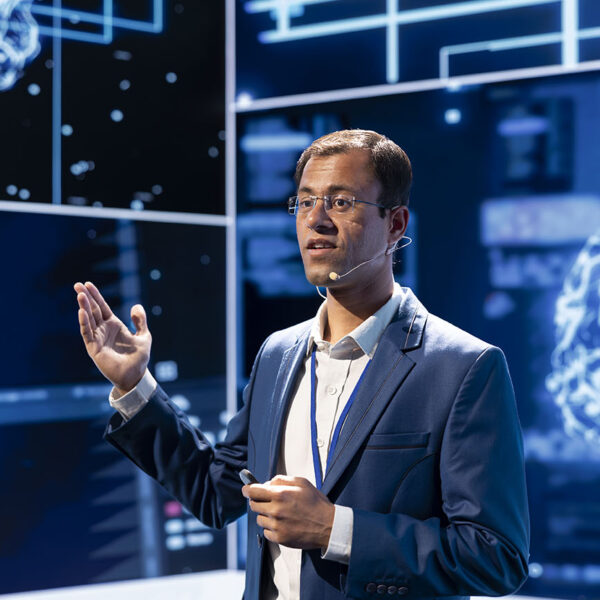 Man speaking at tech expo, exploring latest AI technology trends and case studies. Computer scientist presenting latest artificial intelligence innovations during large event